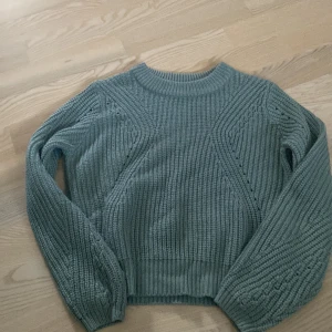 Grön stickad tröja från XOXO Friends - Mysig grön stickad tröja från XOXO Friends med snyggt mönsterstickade detaljer och ribbade muddar. Tröjan har rund halsringning och långa ärmar, perfekt för lager på lager under kyliga dagar.