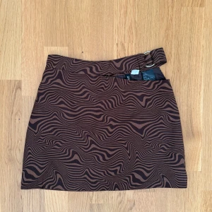 Brun zebramönstrad kortkjol Divided - Snygg brun kortkjol från Divided med zebramönster och coolt bälte i midjan. Kjolen har dragkedja bak och är fodrad för extra komfort. Perfekt för dig som vill sticka ut med ett unikt mönster och trendig vibe.