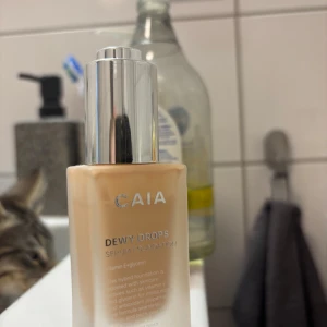CAIA Dewy Drops Serum Foundation 10N - Säljer en CAIA Dewy Drops Serum Foundation i nyansen 10N. Kommer i en lyxig frostad glasflaska med silvrig pump. Ger en fräsch, naturlig finish och innehåller vårdande ingredienser som vitamin E och glycerin. Perfekt för dig som vill ha glow och återfuktning i ett.