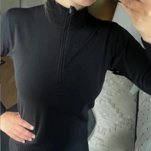 Svart långärmad fleecetröja med half zip - Svart långärmad fleecetröja med hög krage och half zip-dragkedja framtill. Snygg och enkel modell som sitter tight mot kroppen. Perfekt för lager-på-lager och funkar lika bra till jeans som till träningsbyxor.