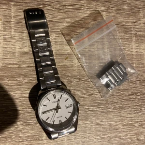 Casio silverfärgad klocka med datum - Stilren Casio klocka i silver med länkarmband i metall och vit urtavla. Klockan har tydliga index, datumvisning och vattentålighet upp till 50 meter. Enkel och klassisk design som passar till allt. Extra länkar medföljer för justering av storlek.