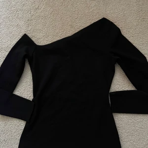 Svart offshoulder klänning H&M - Snygg svart klänning från H&M med offshoulder-design och lång ärm. Tight passform som framhäver figuren, perfekt för dig som gillar stilrena och trendiga plagg. Enkel och elegant look som passar till många tillfällen.