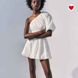 Vit oneshoulder kortklänning - Superfin vit kortklänning med oneshoulder och puffärm. Klänningen har en luftig, lätt struktur och markerad midja som ger en snygg siluett. Perfekt för sommarens varma dagar och när du vill sticka ut lite extra.