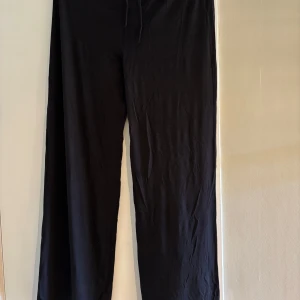 Svarta vida byxor från 157 - Svarta byxor från 157 med breda ben och avslappnad passform. Mjukt material och elastisk midja med snörning för extra komfort. Perfekta för en chill look och enkla att matcha med allt.