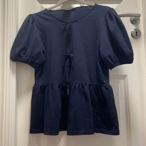Mörkblå blus med puffärm Gina Tricot - Supersöt mörkblå blus från Gina Tricot med puffiga korta ärmar och två knyt framtill. Blusen har en volang nedtill  och är gjord i mjuk bomull. Aldrig använd och storlek 170❤️skriv för frågor