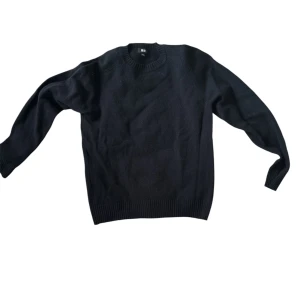 Svart stickad tröja med rund hals - En klassisk svart stickad tröja med rund halsringning och ribbade muddar vid ärmslut och nederkant. Perfekt för lager-på-lager och enkel att matcha med olika outfits. Långärmad och i en normal passform.