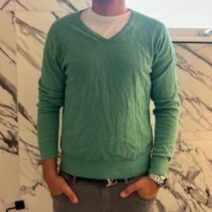 Grön v-ringad tröja Tommy Hilfiger - Snygg grön v-ringad tröja från Tommy Hilfiger i storlek L. Tillverkad i en skön blandning av linne och bomull, perfekt för dig som gillar en stilren look. Tröjan har långa ärmar och ribbade muddar för en klassisk passform.