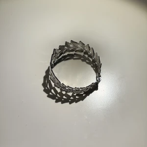 Silverfärgat armband med bladmotiv - Snyggt armband i silverfärg med detaljerade blad runt hela bandet. Ger en cool och unik look, perfekt för dig som gillar naturinspirerade accessoarer. Armbandet har en öppen design som gör det lätt att ta på och av.