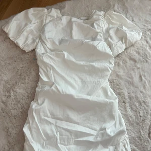 Vit kort puffärmad klänning NLY Trend - Supersöt vit kortklänning från NLY Trend med puffiga korta ärmar och figurnära passform. Klänningen har dragkedja i ryggen och är gjord i ett lätt, slätt material. Perfekt för dig som vill ha en clean och trendig look.
