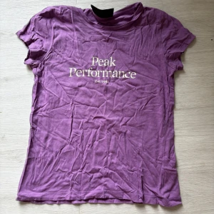 Lila Peak Performance t-shirt - Snygg lila t-shirt från Peak Performance med vit logga framtill. Klassisk passform och rund halsringning, perfekt för en avslappnad stil. Tillverkad i mjuk bomull som känns skön mot huden.