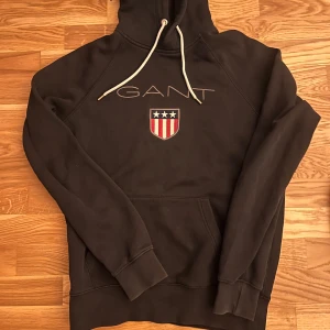 Svart  från GANT med logga - Svart  från GANT med broderad logga och sköld på bröstet. Hoodien är i storlek M🤩🙌