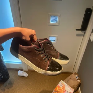 Lanvin vinröda - Säljer ett par vinröda sneakers från Lanvin med snygg lackad tå och vita sulor. Skorna har svarta skosnören och ovandel i mocka. Klassisk och stilren design som passar till mycket. Skorna är i bra skick men fixade med whitening cream på sulan! Tveka inte på att fråga frågor! Priset är ej hugget i sten. 