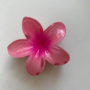 Rosa blomformad hårklämma - Superfin hårklämma i form av en blomma i glansig rosa plast. Perfekt accessoar för att ge din frisyr en söt och färgglad touch. Klämman har fem blomblad och är riktigt iögonfallande. Passar perfekt till sommarens alla looks!