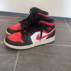 Nike Air Jordan 1 svart/röd/vit - Säljer ett par ikoniska Nike Air Jordan 1 sneakers i svart, rött och vitt. Klassisk mid-top modell med svart snörning, röd tå och häl, vit sidopanel och röd swoosh. Ovandel i skinn och textil, med rund tå och platt sula. Perfekta för dig som gillar streetstyle. Köpta från zalando med värde över 1000 kr.