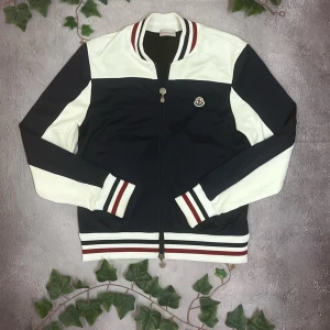 Moncler Cardigan (Äkta) - Moncler Cardigan 🎨 Färg: Mörkblå, vit och röd 📏 Storlek: Storlek 2, motsvarar storlek Medium (M) 📐 Mått: Fråga ifall det önskas! ♻️ Skick:9/10