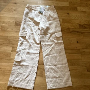 Beiga cargopants  från H&M - Stilrena beiga cargopants från H&M. Vida ben och flera praktiska fickor på sidorna ger en avslappnad vibe. Aldrig använt, prislapp finns kvar