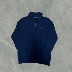 Marinblå stickad tröja Polo Ralph Lauren - Säljer en snygg marinblå kabelstickad half zip från Ralph Lauren med dragkedja och klassiskt kabelstickat mönster. Tröjan har en liten röd broderad logga på bröstet och ribbade muddar. Perfekt för kyliga dagar! Den är i superfint skick endast använd ett par gånger. Storlek M men kan även passa en större S. Vid några frågor eller funderingar är det bara att höra av sig.