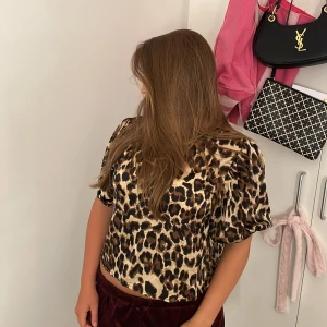 Leopardmönstrad blus med knyt bak -  MAN KAN HA ROSET DÄR FRAMME OXÅ, DEN ÄR FÖR BÅDA HÅLLEN) Säljer en kortärmad blus med leopardmönster i beige, brun och svart. Toppen har en croppad passform och snygg knytning i svart band baktill som ger en öppen rygg. Perfekt för dig som vill sticka ut med ett djurmönster och coola detaljer. KÖPTE FÖR 649kr