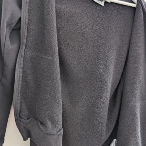 Svart fleecejacka från Andy by Frank Dandy - Svart fleecejacka med huva från Andy by Frank Dandy. Jackan har dragkedja framtill, ribbade muddar och är tillverkad i mjukt fleecematerial. Perfekt för kyliga dagar när du vill vara både bekväm och stilren.