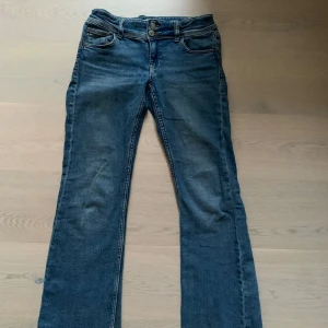 Blå bootcut jeans med dubbla knappar - Snygga mörkblå blå jeans med bootcut passform! Jeansen har en fin detalj med två knappar framtill vid midjan. På baksidan av byxorna finns det även två fickor med knappar. Jeansen är bara andvända ett fåtal gånger. Byoxorna är perfekta för dig som gillar en avslappnad men trendig stil!