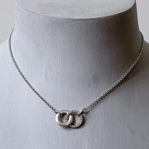 Silverhalsband esprit  - Stilrent halsband i silver med två sammanlänkade ringar, varav en är slät och den andra dekorerad med små gnistrande stenar. Kedjan är tunn och smidig med diskret lås och liten bricka märkt 925. Perfekt för dig som gillar minimalistiska smycken med en twist.