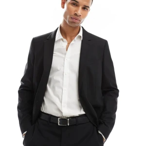 Svart klassisk kostymkavaj herr - Snygg svart kavaj med klassisk passform och tre knappar vid ärmslutet. Stilren design med spetsiga slag och diskret bröstficka. Perfekt till skjorta och byxa för en clean look. Materialet känns mjukt och följsamt.