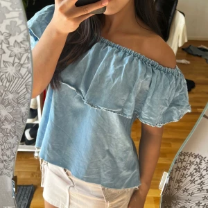 Ljusblå jeans offshoulder topp med volang - Superfin ljusblå jeans offshoulder topp med bred volang runt hela axelpartiet. Tunn och luftig, perfekt för varma dagar. Snygg till både shorts och kjol för en chill sommarlook.
