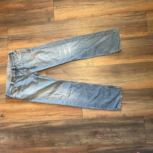 Blå raka jeans från Diesel - Snygga blå jeans från Diesel med raka ben och slitna detaljer. Jeansen har klassisk femficksdesign, broderade bakfickor och råa kanter vid benslut. Perfekta för en avslappnad streetstil och tillverkade i mjuk bomullsdenim.
