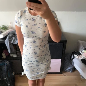 Vit blommig kortklänning från SHEIN - Supersöt vit kortklänning från SHEIN med blått blommönster. Klänningen är ribbad, har korta ärmar och en figurnära passform. Perfekt för sommarens alla tillfällen och enkel att styla med sneakers eller sandaler.