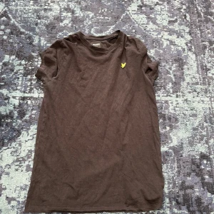 Svart t-shirt från Lyle & Scott - Snygg svart t-shirt från Lyle & Scott med klassisk passform och korta ärmar. T-shirten har en gul broderad logga på bröstet och är gjord i mjuk bomull. Perfekt för en chill och stilren look.