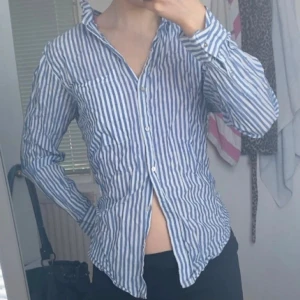 Blåvit randig skjorta Gina Tricot - Snygg blåvit randig skjorta från Gina Tricot i 100% ekologisk bomull. Skjortan har klassisk krage, knäppning framtill och långa ärmar med manschett. Perfekt för en chill och stilren look.