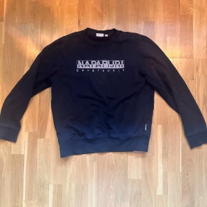 Svart sweatshirt från Napapijri - Svart sweatshirt från Napapijri med tryckt logga på bröstet. Klassisk rund halsringning och långa ärmar.