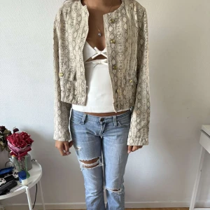 Beige denim jacka med ormmönster och guldknappar - Snygg beige denim jacka med ormmönster och guldiga knappar framtill. Jackan är croppad och har två fickor med lock. Långärmad och rak passform, jackan kan användas som jacka under sommaren men som blus till hösten! 🌸🌸helt ny! Aldrig använd!!