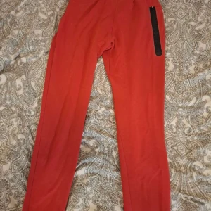 Röda mjukisbyxor från Nike - Snygga röda mjukisbyxor från Nike med svart logga på låret och dragkedjeficka på sidan. Har några märken så säljer för låg pris
