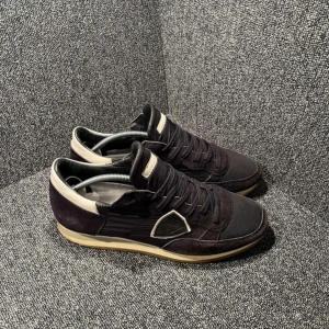 Svarta sneakers från Philippe Model - Snygga svarta sneakers från Philippe Model med beige detaljer och gummisula. Ovandelen är i mocka och textil, med klassisk snörning och rund tå. Perfekta för dig som gillar stilrena och sportiga skor med en exklusiv touch.