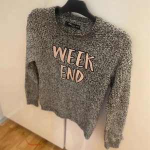 Gråmelerad stickad tröja WEEKEND strl XXS  - Stickad tröja från Resteröds i gråmelerat garn med svart och vitt. Stor text 'WEEKEND' i ljusrosa framtill. Klassisk rund halsringning och långa ärmar. Perfekt för chill dagar och snygg till jeans.