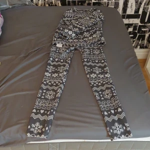Svarta leggings med vintermönster S - Mysiga svarta leggings med vita snöflingor, hjärtan och zigzag-mönster. Perfekta för kalla dagar, stretchiga och sköna med elastisk midja. Materialet är 98% polyester och 2% elastan för extra komfort. Storlek S men funkar också på kroppar som har normalt xs