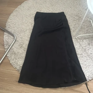 Svart långkjol från Zara XS - Säljer en stilren svart långkjol från Zara i storlek XS. Kjolen har en klassisk rak passform och är tillverkad i satin. Perfekt att styla med sneakers eller boots för en clean look. Säljer denna pga att den är för kort för mig, användes mycket förra sommaren! 