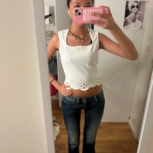 Vit ribbad linnetopp med broderad kant - Supersöt vit croppad linnetopp med fyrkantig ringning och broderade blommor längs den vågiga nederkanten. Ribbad struktur och ärmlös design gör den perfekt för varma dagar. Enkel att styla med jeans eller kjol för en fräsch look.