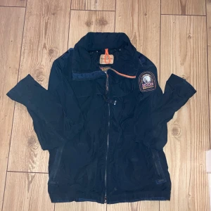 Svart jacka från Parajumpers - Säljer en svart jacka från Parajumpers med en cool patch på ärmen. Jackan har dragkedja och en snygg orange detalj vid kragen. Perfekt för höst och vår! Säljer för superpris🌟🌟