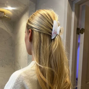 Vit hårklämma med rosa pärlor - Snygg vit hårklämma med skimrande yta och dekorerad med rosa pärlor som bildar ordet 'Joy' med en söt genomskinlig rosett. Perfekt för att ge en extra touch till din frisyr. Oanvänd, endast testad för bilden!