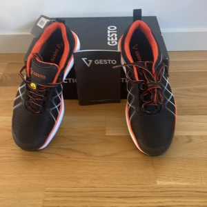 Svarta sneakers från Gesto - Helt nya med prislapp.Snygga svarta sneakers från Gesto med orange detaljer och vit sula. Skorna har snörning och en sportig design som passar perfekt för träning eller vardagsbruk. Den svarta färgen kombineras med orange insida och detaljer för en fräsch look. Kan duskutera priset.