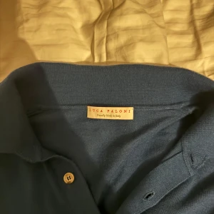 Mörkblå kaschmir pikétröja från Luca Faloni - Säljer en elegant mörkblå pikétröja från Luca Faloni. Tröjan har en klassisk krage och knappar framtill. Perfekt för en stilren look. Endast använd 3-4 gånger, nyskick. Ingen prislapp eller kvitto. Bra pris