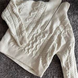 Beige stickad tröja från Bik Bok - Mysig beige stickad tröja från Bik Bok med kabelstickat mönster och dragkedja framtill. Perfekt för kyliga dagar med sin varma och bekväma design. Tröjan har långa ärmar och ribbade kanter.