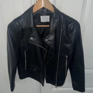 Svart skinnjacka från Zara - Snygg svart skinnjacka från Zara med dragkedja och knappar. Jackan har en klassisk bikerstil med två framfickor med dragkedja och en knappficka. Perfekt för en cool look! Pris kan diskuteras💞