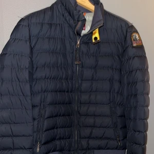 Mörkblå dunjacka från Parajumpers - Säljer en mörkblå dunjacka från Parajumpers. Jackan är superlätt och har en dragkedja framtill. Den har en hög krage med en gul detalj och ett märke på ärmen. Perfekt för kyliga dagar. En på nypris kostar 5700. Barnstorlek