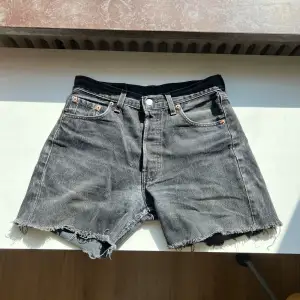 Säljer ett par svarta jeansshorts från Levi's, modell 501. De har en klassisk femficksdesign och knappgylf. Shortsen har en rå kant med fransar för en avslappnad look. DIY shorts med distressed look. Perfekta för sommaren!