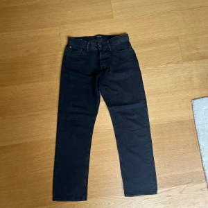 Svarta jeansbyxor Loose/Chris - Säljer ett par svarta jeansbyxor med en loose passform. Byxorna har en klassisk design med fem fickor och knappgylf. Perfekta för en avslappnad stil.