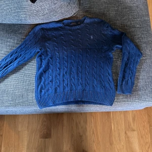 Blå kabelstickad tröja från Polo Ralph Lauren - Säljer en snygg blå kabelstickad tröja från Polo Ralph Lauren. Tröjan har en klassisk design med rund hals och långa ärmar. Perfekt för kyligare dagar. 🧶💙Pris går alltid att förhandla!