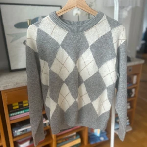 Grå och vit tröja från Uniqlo - Säljer en stilren grå tröja från Uniqlo med ett klassiskt rutmönster i vitt. Tröjan har långa ärmar och en rund halsringning, perfekt för en avslappnad look. Tillverkad i Vietnam.